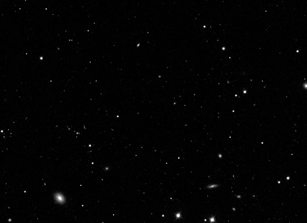 A greyscale telescope image of faint stars and galaxies in Coma Berenices, overlaid with the right ascension and declination grid that arcsec solved for it. The field is 13.5′ × 9.8′, centred on RA 12h59m32s, Dec +27°27′58″.
